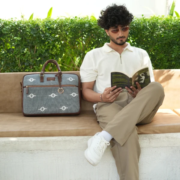 Slate grey handwoven rug laptop bag with white eye-shaped geometric patterns and brown vegan leather handles.