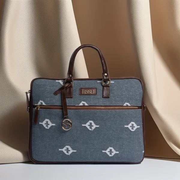 Grey handwoven rug laptop bag with white eye-shaped geometric motifs and premium brown vegan leather handles.