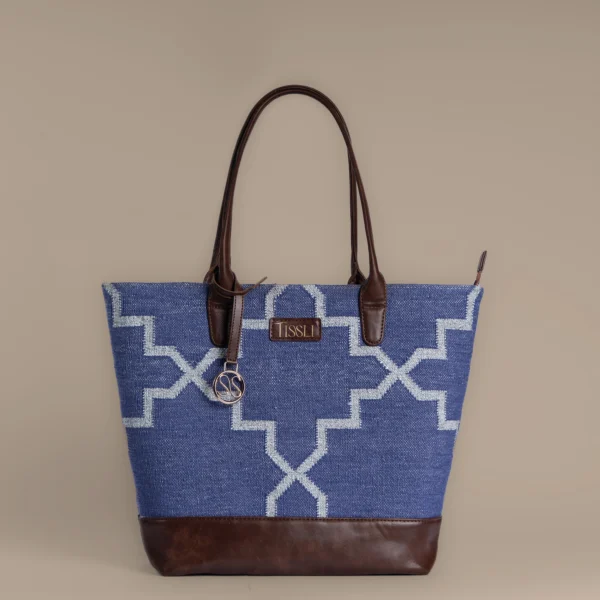 Handwoven indigo blue rug tote bag with silver geometric trellis pattern and brown leather base by Tissli.