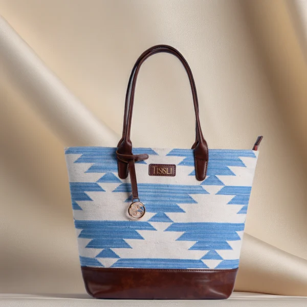 Handwoven blue and white geometric rug tote bag with brown leather base and handles by Tissli.