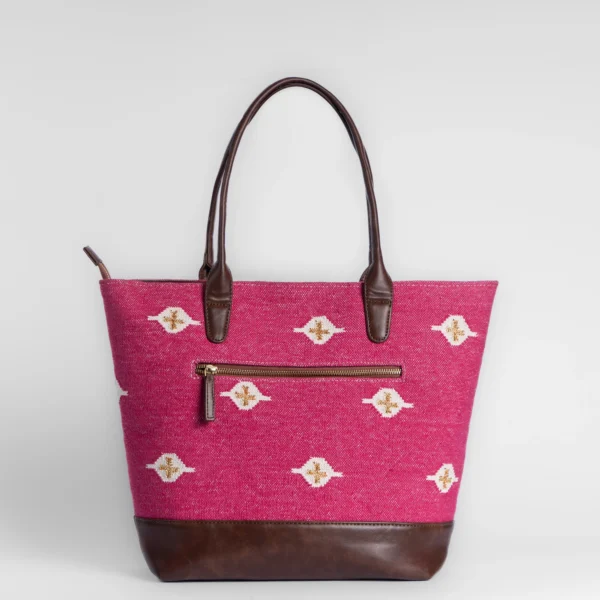 Tissli magenta handwoven rug tote with white and gold eye motifs, brown leather base, and gold brand charm.