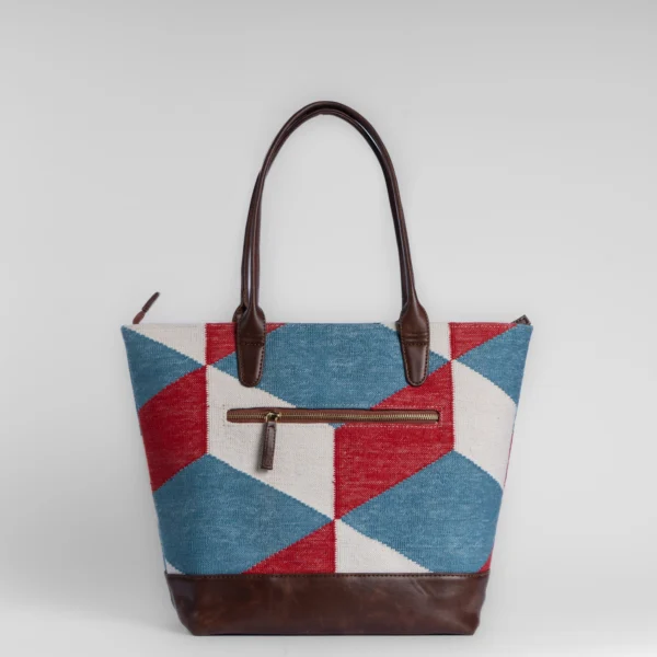 Geometric red, blue, and white handwoven rug tote bag with brown vegan leather trim and Tissli brass monogram.