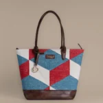 Handwoven red, blue, and white geometric rug tote bag with brown vegan leather base and Tissli brass charm.