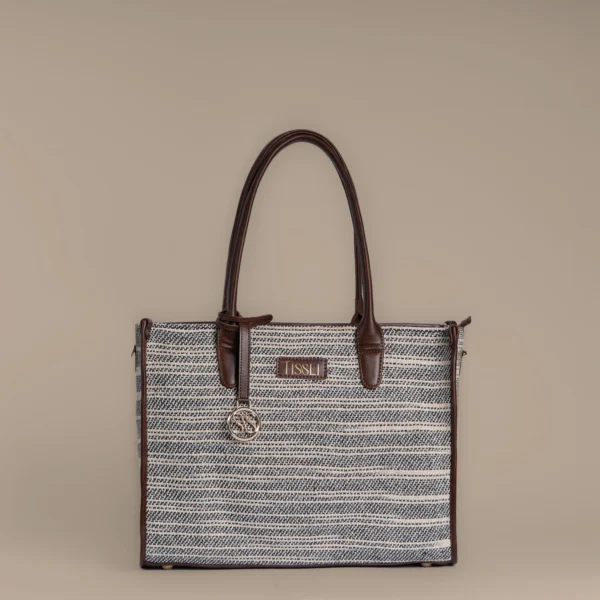 Structured charcoal and cream handwoven rug tote bag with brown leather trim and Tissli gold logo.