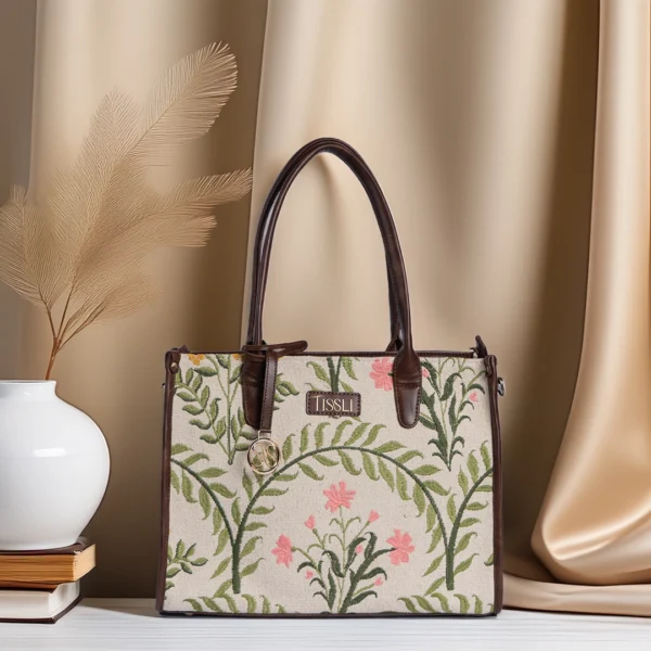 Structured cream handwoven rug tote with pink floral and green fern embroidery and brown leather handles by Tissli.