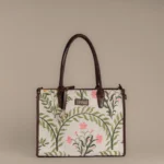 Front view of Tissli Tote showing detailed floral embroidery on a cream handwoven rug base.