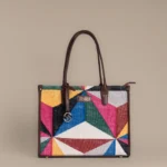 Structured multicoloured geometric rug tote bag with sunburst pattern and brown leather handles by Tissli.