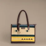 Structured mustard and green handwoven rug tote with tribal motifs and brown leather handles by Tissli.